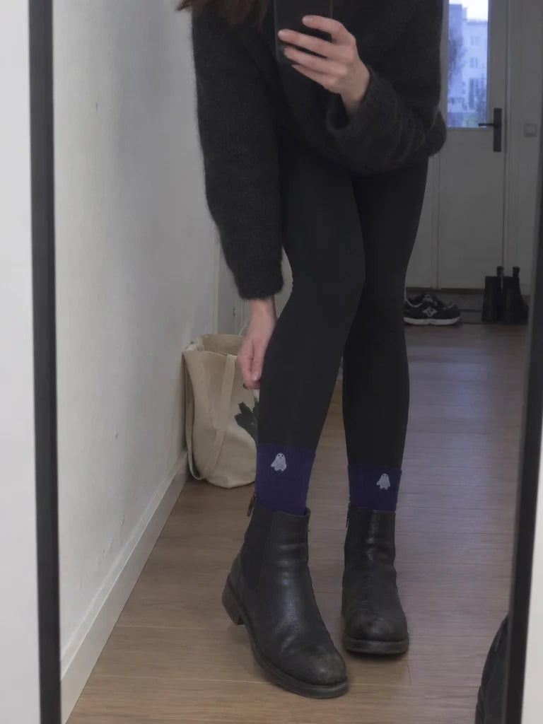 A customer's own mirror photo in a narrow apartment hall: the deep purple mid-calf Halloween socks f